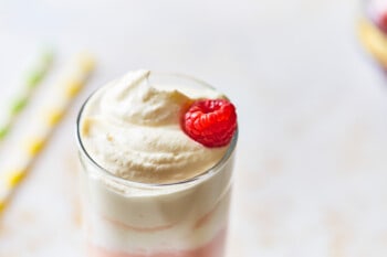 a single raspberry on top of whipped cream topped boozy raspberry italian cream soda in a tall glass.