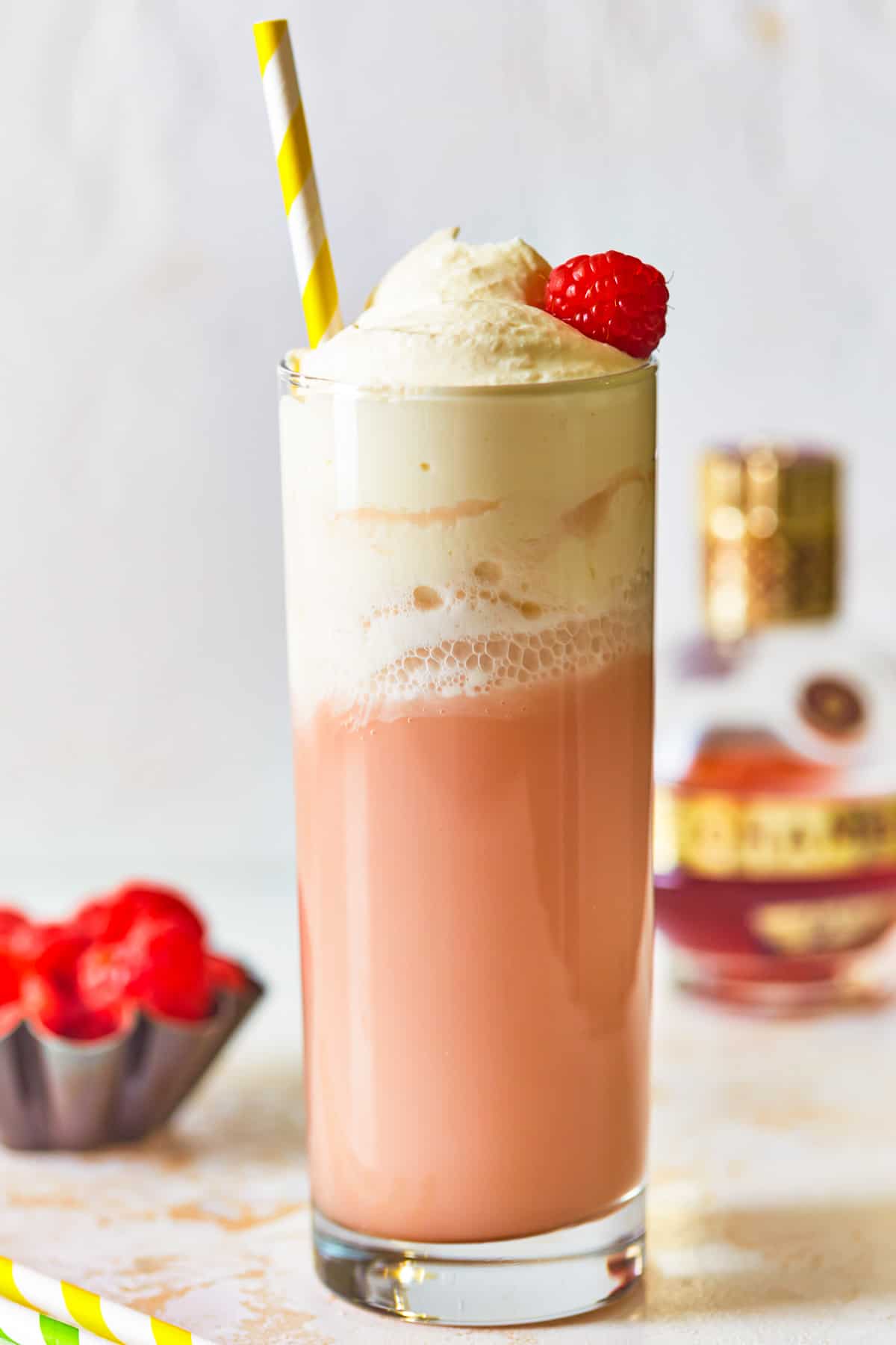 side view of raspberry italian cream soda in a tall glass topped with whipped cream, a raspberry, and a straw.