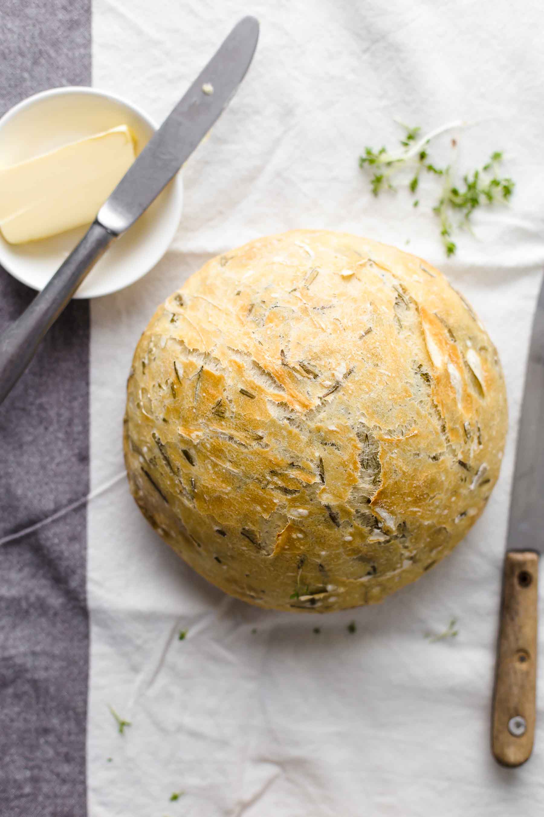 round loaf of rosemary bread next to a small dish of butter