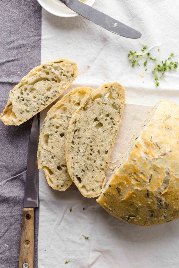 A Dutch oven bread loaf with herbs on a cutting board.