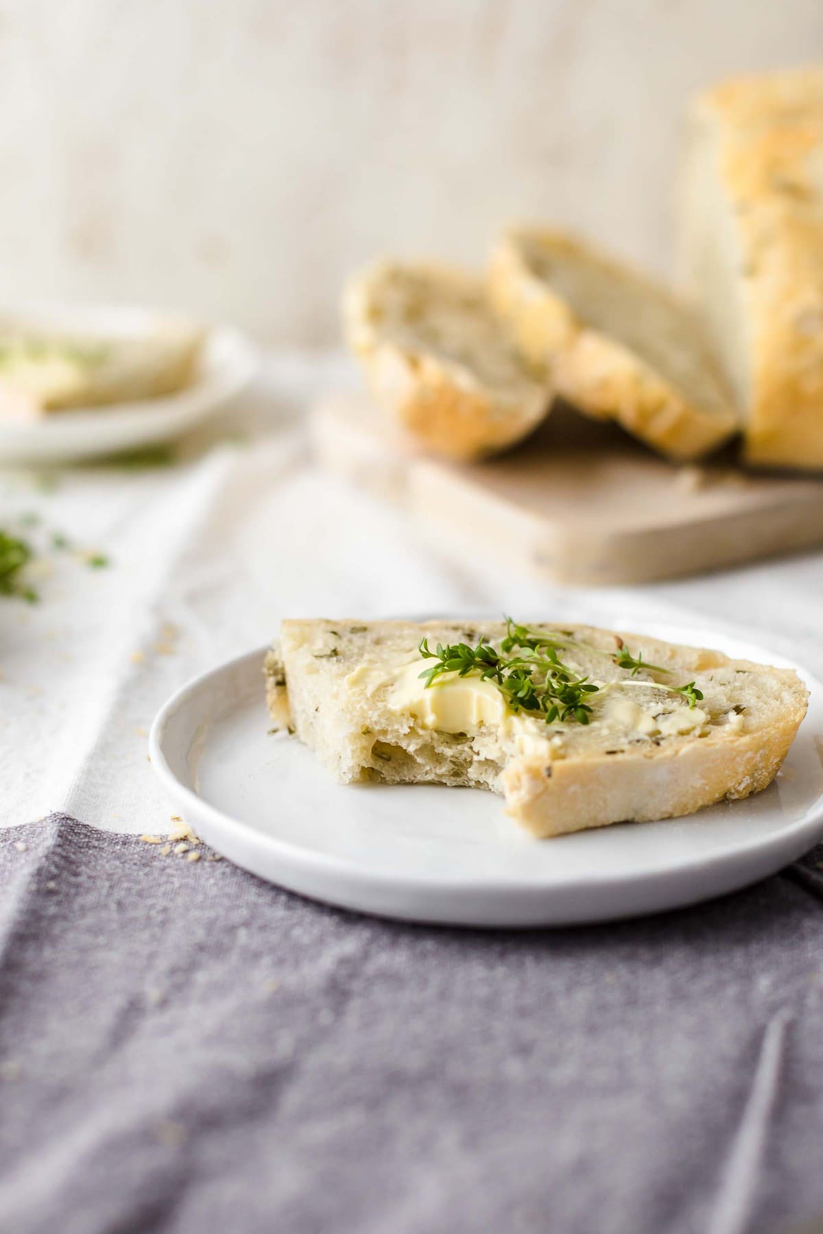 a slice of rosemary bread on a small white plate topped with butter 