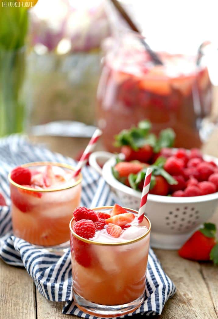 Sangria glasses in front of a bowl of red berries and a pitcher