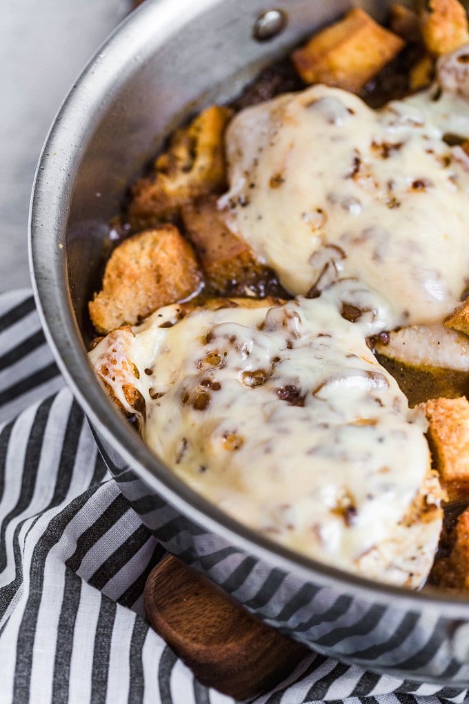 Chicken breast covered in cheese, with croutons in a skillet