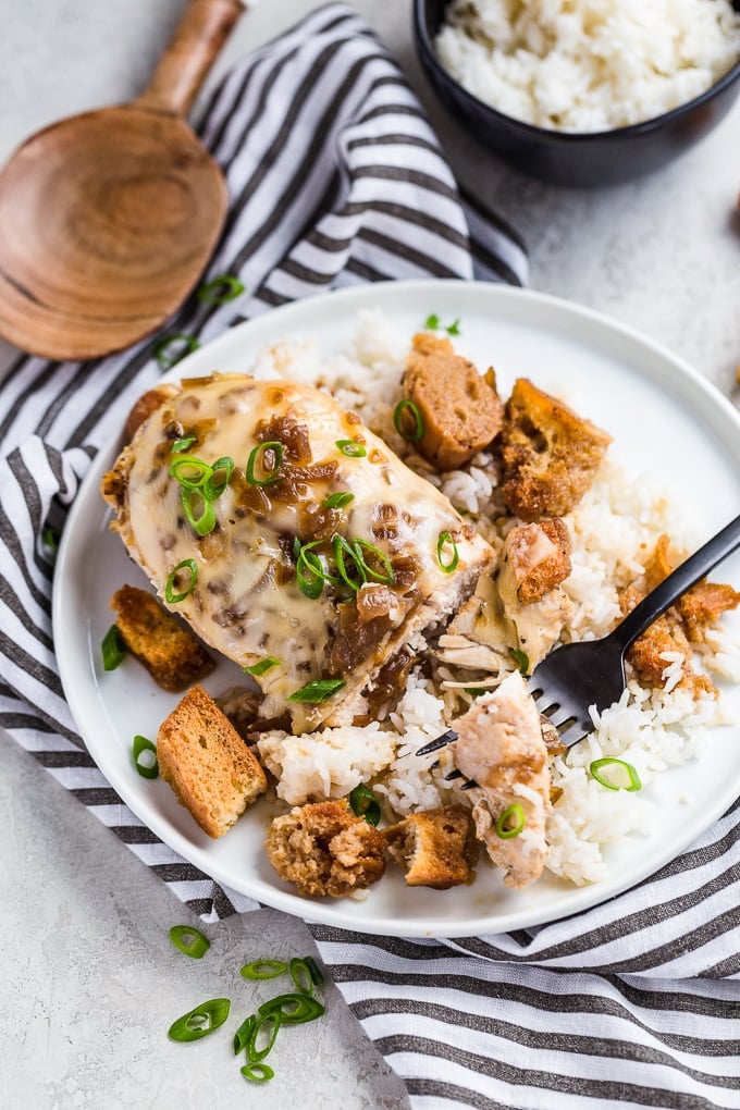 Chicken breast covered in cheese, on a white plate with white rice and croutons