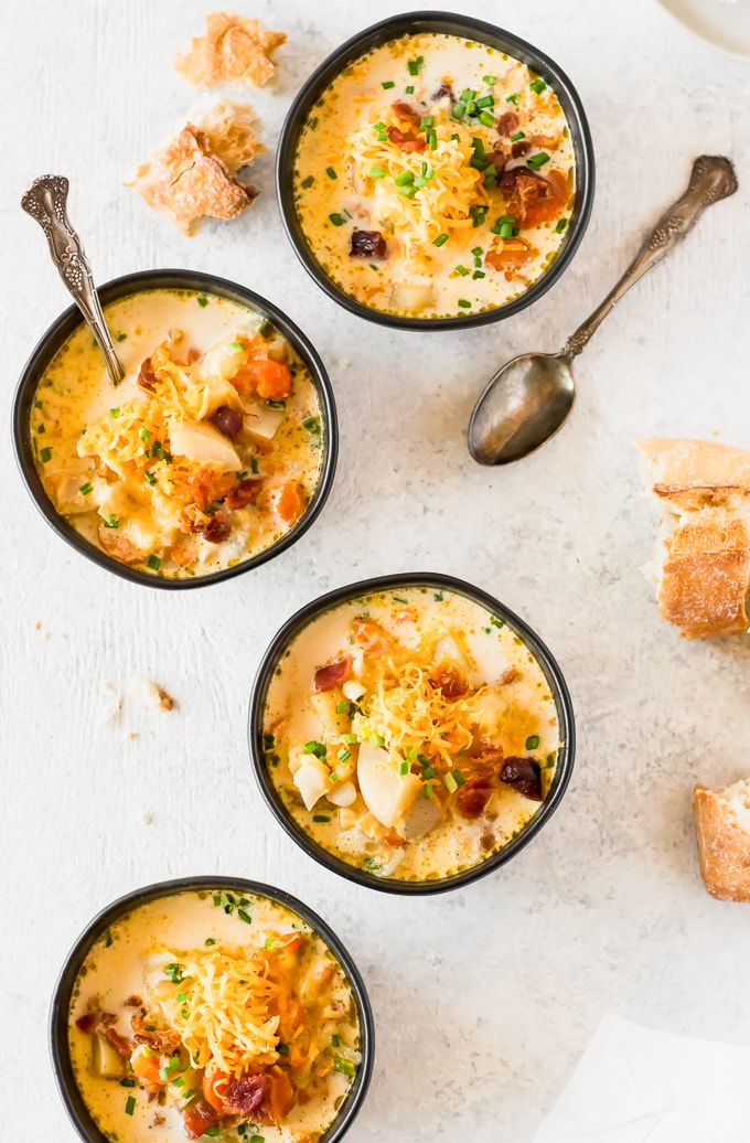 four bowls of soup topped with bacon, cheese, and more