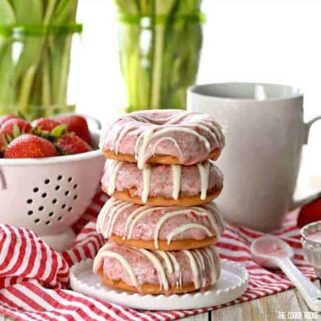 Strawberries and Cream Cake Mix Donuts on a plate in front of a coffee mug and colander of strawberries