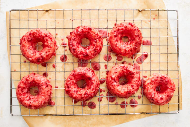 overhead view of 7 strawberry donuts dipped in glaze drying on a wire cooling rack.