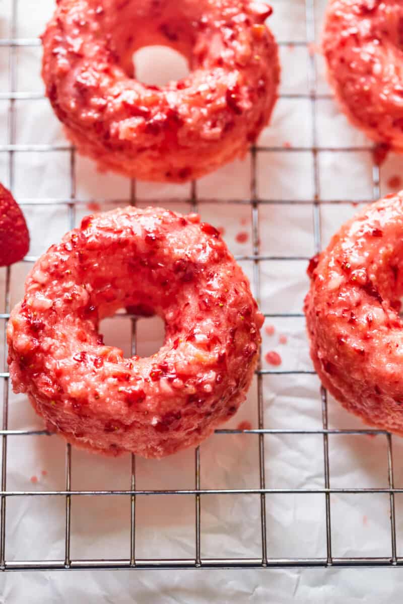 three-quarters view of strawberry donuts on a wire cooling rack.