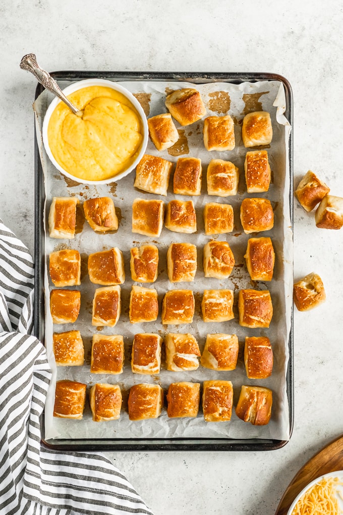 pretzel bites lined up on cookie sheet with cheese dip in bowl