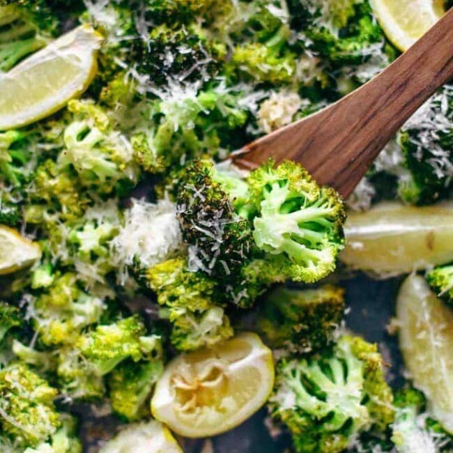 broccoli on a baking dish with lemon wedges and parmesan