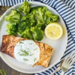 grilled salmon on a white plate with lemon and broccoli.