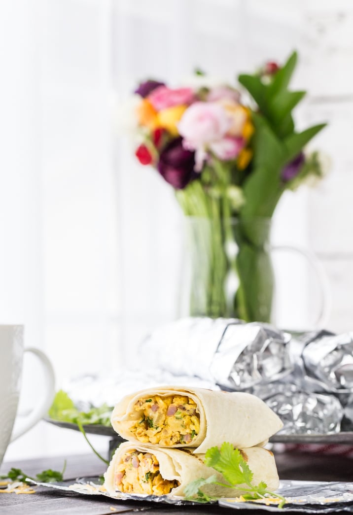 stacked breakfast burritos in front of a vase of flowers