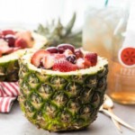 two pineapple bowls filled with fruit and a drink.