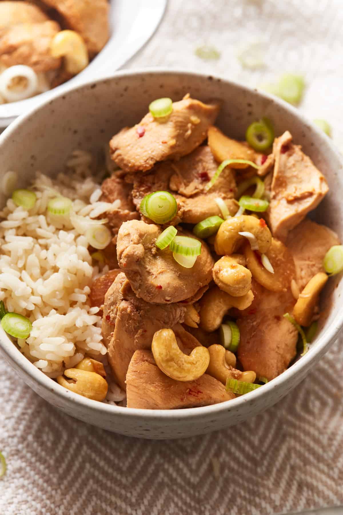 three-quarters view of crockpot cashew chicken in a tan bowl with rice.