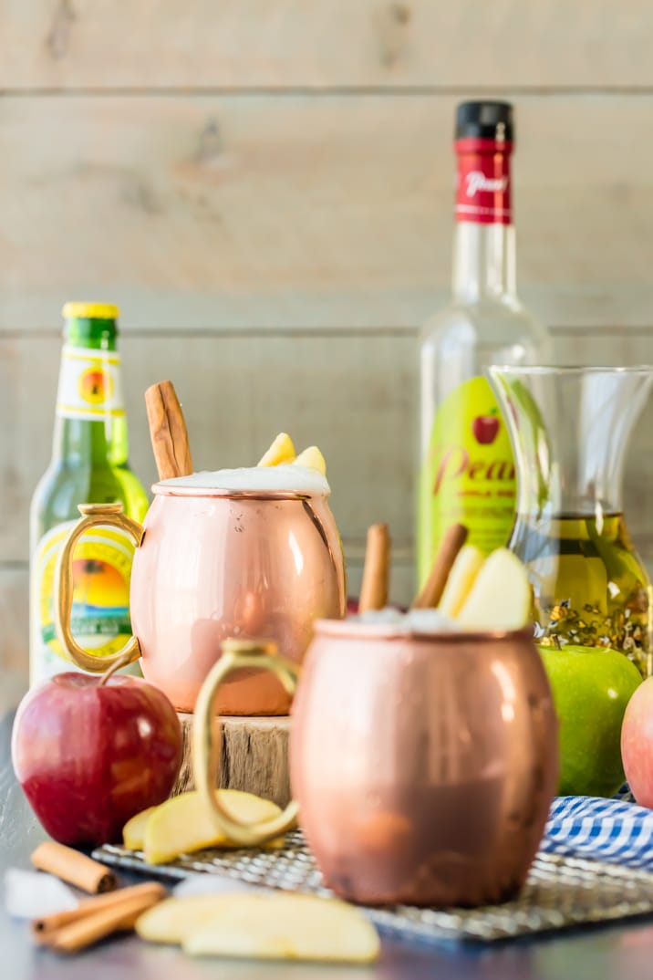 moscow mules on a table with apples, beer bottles, and cinnamon sticks