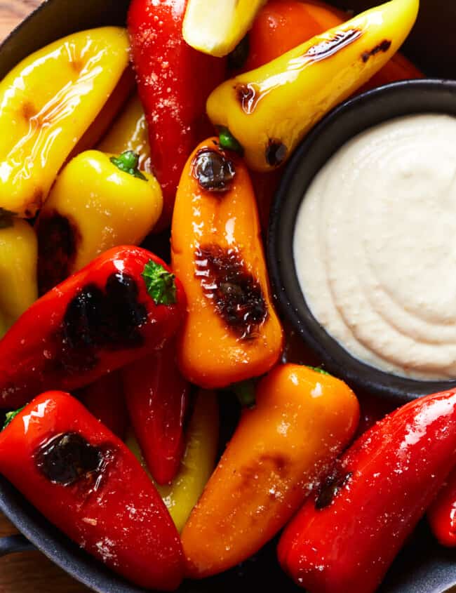 overhead view of tricolor blistered sweet peppers in a black bowl with goat cheese dip.