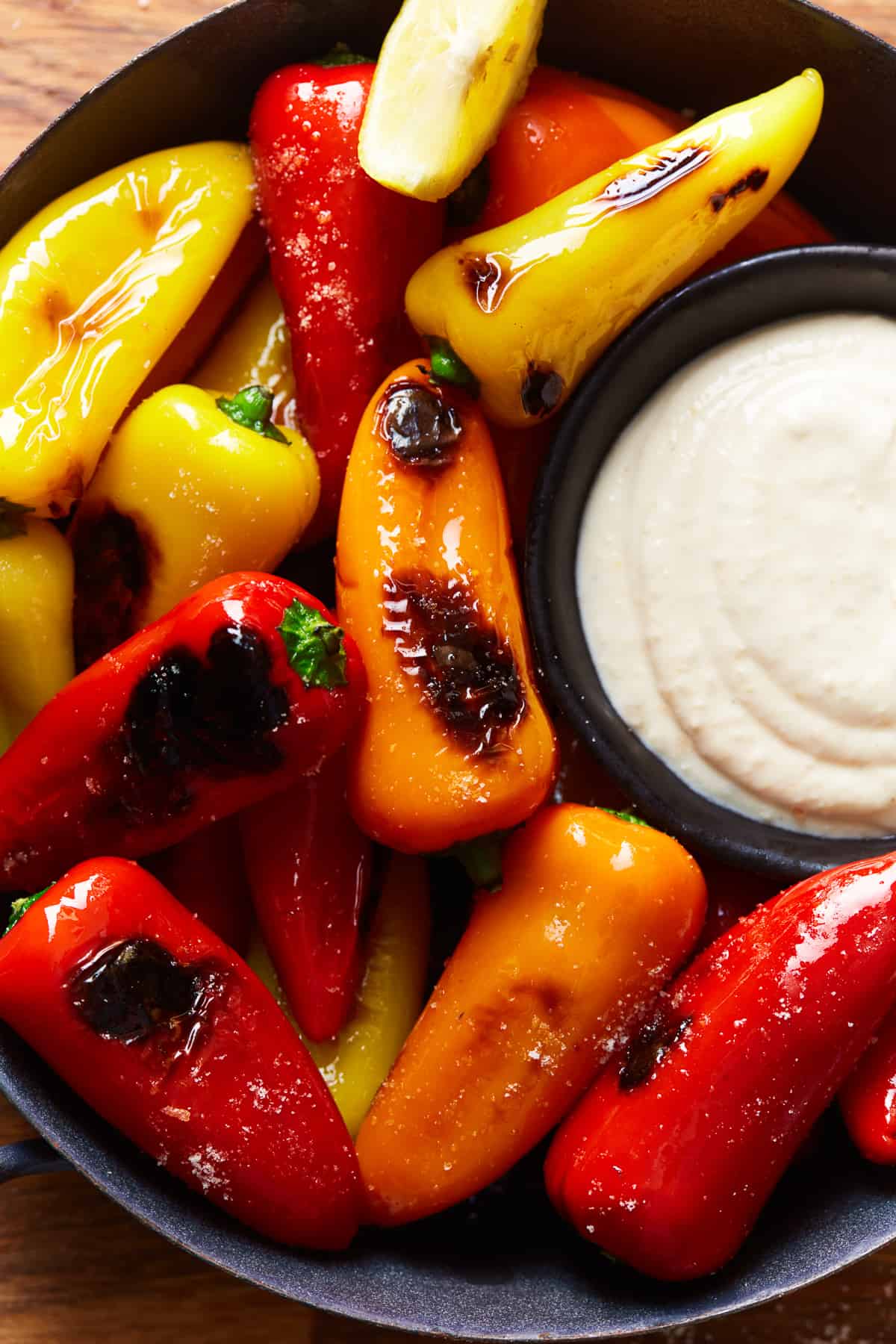 overhead view of tricolor blistered sweet peppers in a black bowl with goat cheese dip.