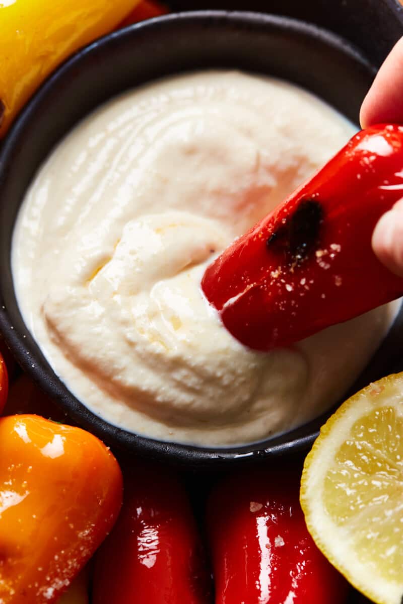 a red blistered sweet pepper being dipped in goat cheese dip.