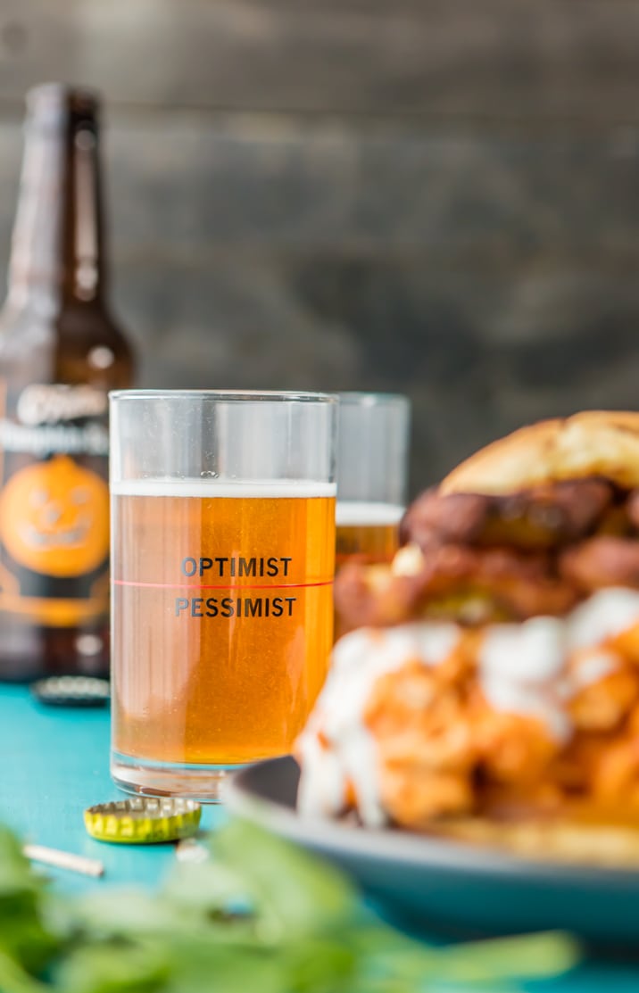 glass of beer in focus, buffalo chicken sandwich blurred in the foreground