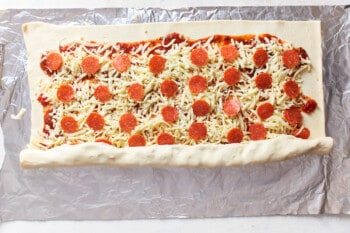 sauce, cheese, and pepperoni on dough being rolled into a log.
