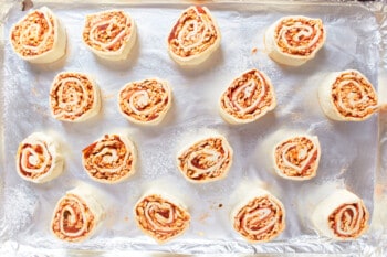16 pepperoni pizza rolls on a lined baking sheet.