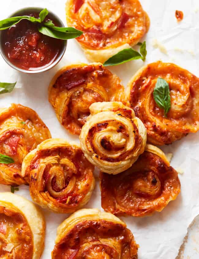 overhead view of pepperoni pizza rolls on parchment paper next to a small cup of marinara sauce.