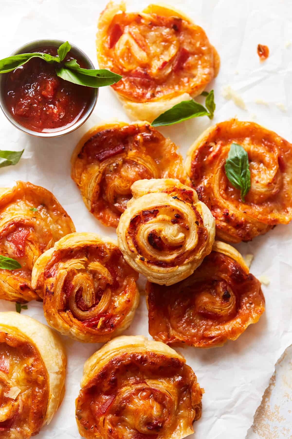overhead view of pepperoni pizza rolls on parchment paper next to a small cup of marinara sauce.