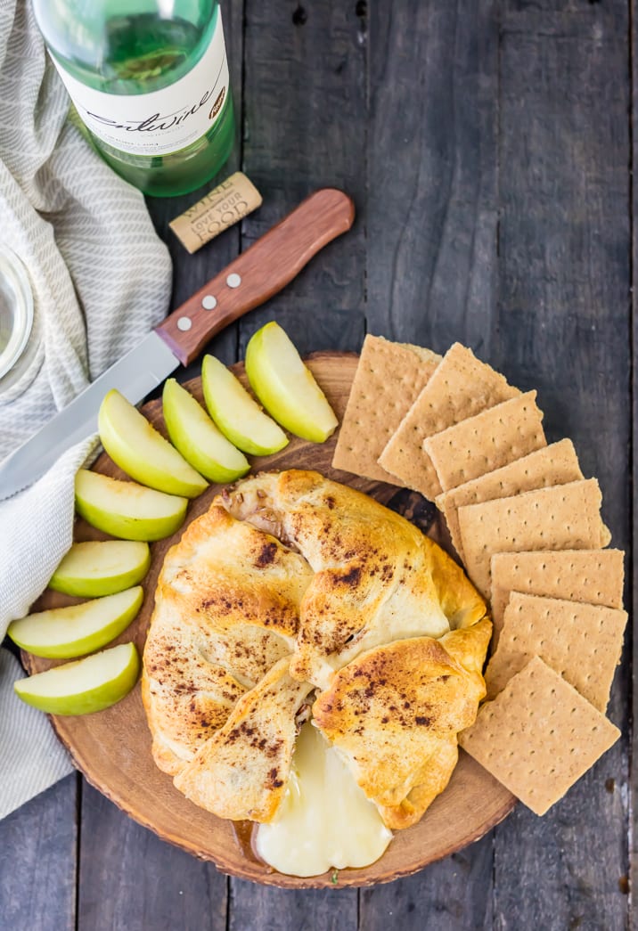 apple pie baked brie with apple slices and graham crackers on wooden plate