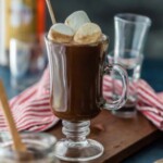 chocolate hot buttered rum in a glass mug topped with big marshmallows sitting on a table