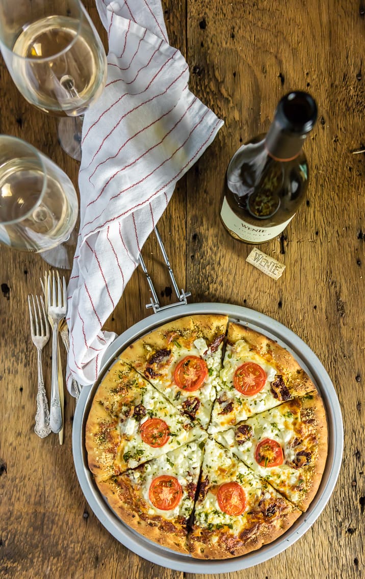 easy gourmet white pizza, bottle of wine and two glasses, napkin on wood table