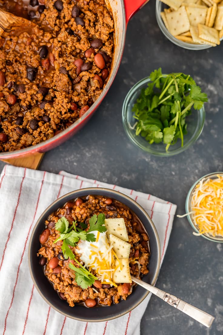 overhead view of a bowl of chili next to a large pot of chili and small bowls of toppings