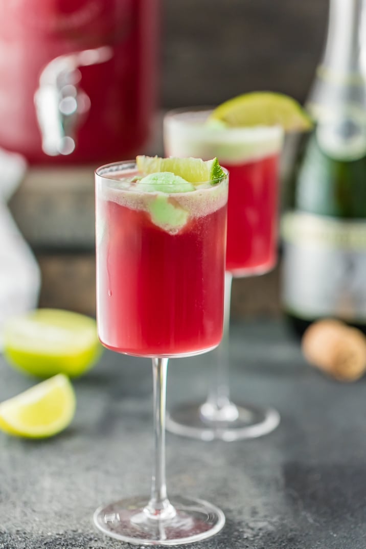 two glasses of cranberry limeade holiday champagne punch with lime garnish