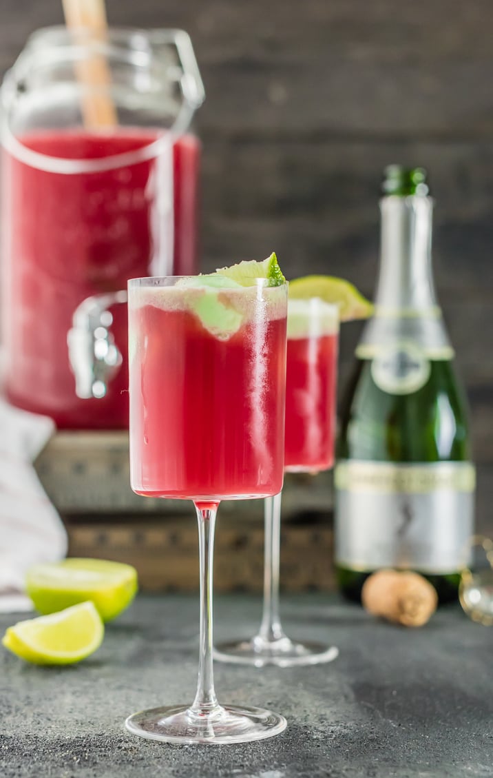 two glasses of cranberry limeade holiday champagne punch with pitcher and bottle in background