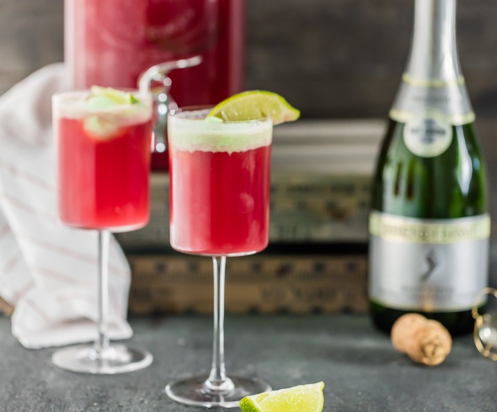 two glasses of cranberry limeade holiday champagne punch with bottle and cork