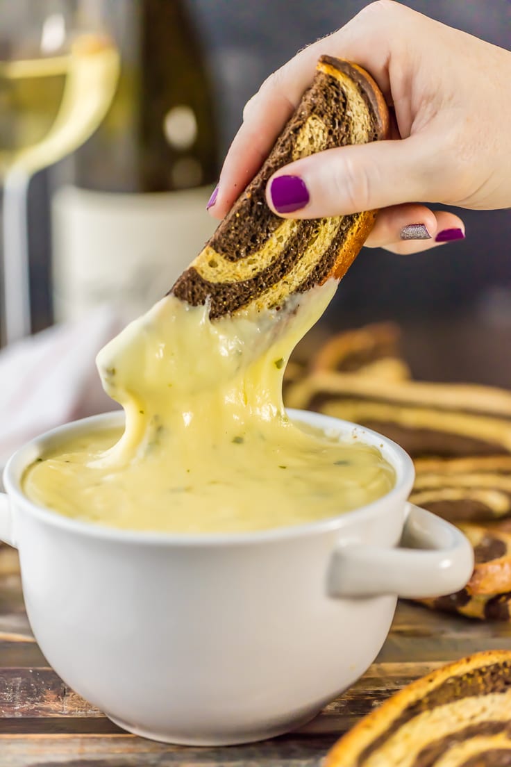 SUPER EASY WHITE WINE FONDUE! Made with swiss, gouda, and of course white wine. Easy, cheesy, melty, and delicious recipe! Made in minutes! Served with marbled rye crostini!