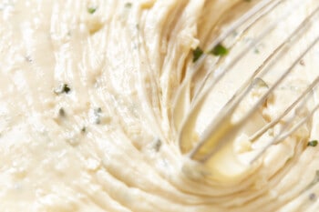 close up of basil being stirred into white wine fondue with a whisk.