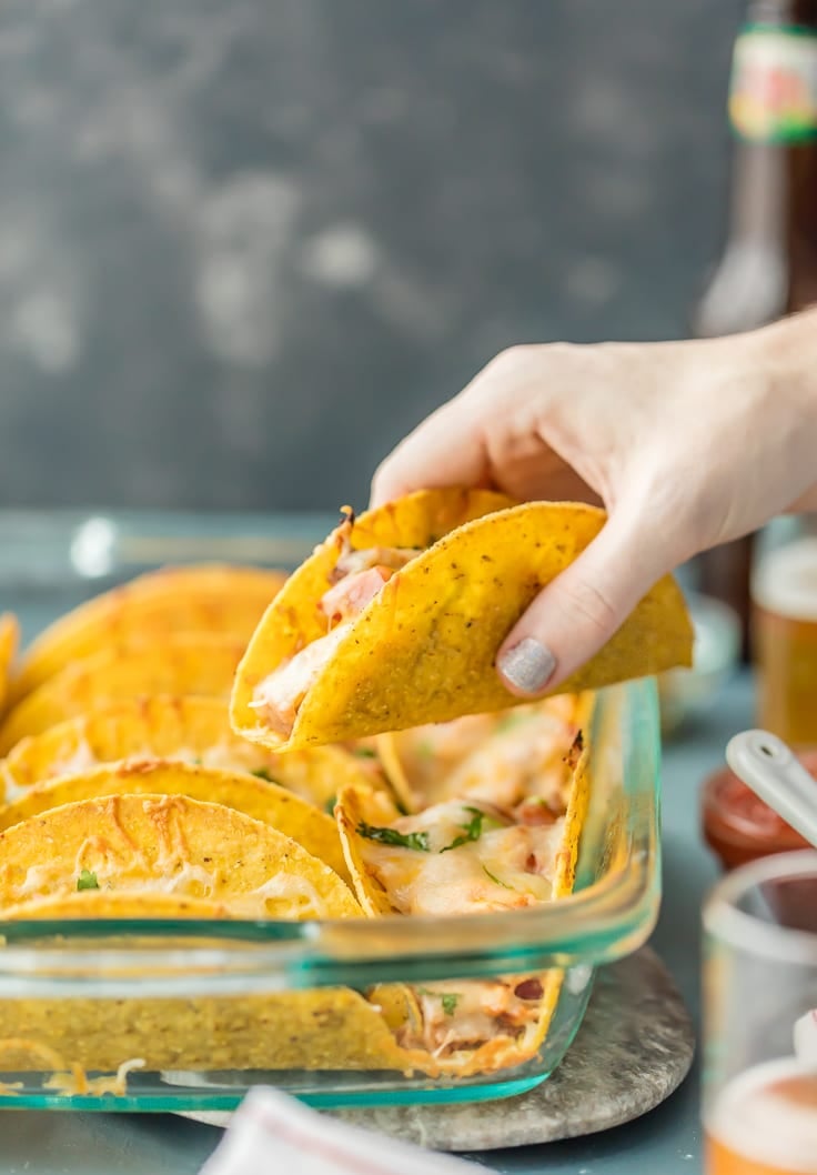 Chicken Tacos are the PERFECT quick weeknight dinner! OVEN BAKED chicken tacos have lots of flavor and none of the stress. BEST CHICKEN TACOS recipe ever. hand picking up taco from a baking dish