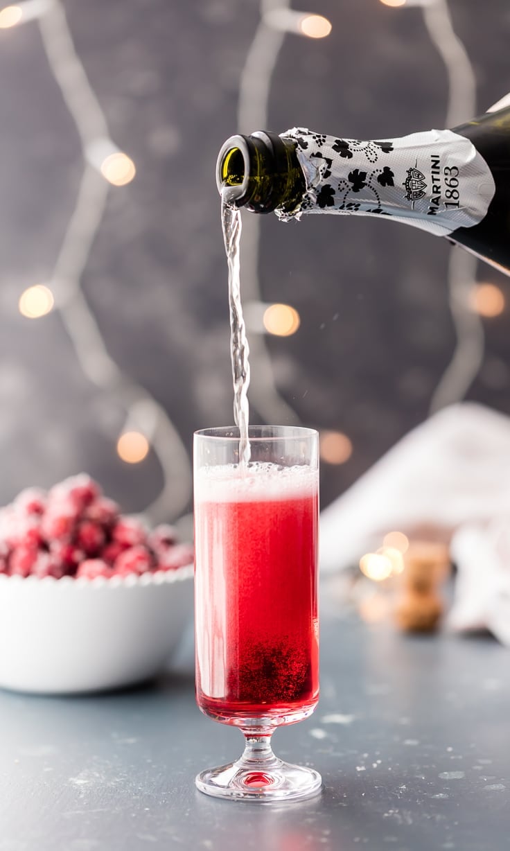 pouring champagne into glass ofcranberry ginger mimosas