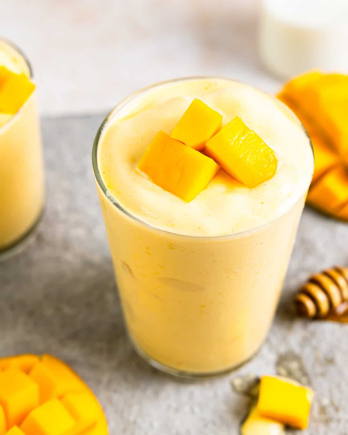 three-quarters view of a mango smoothie in a glass with mango chunks on top.