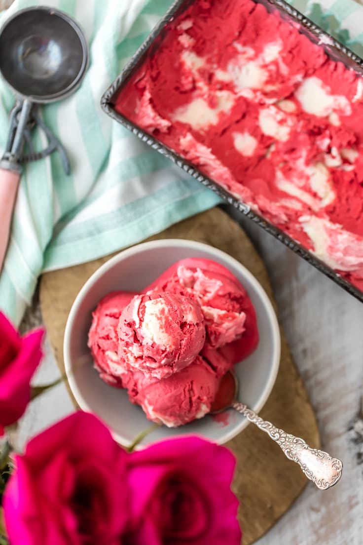 scoops of red velvet cream cheese ice cream in a bowl, next to a large container of the red and white ice cream