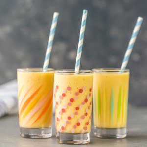 three simple mango smoothies in patterned glasses with straws