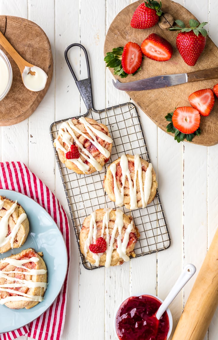 strawberry cinnamon roll cookies on a cooling rack, surrounded by plates of cookies and strawberries