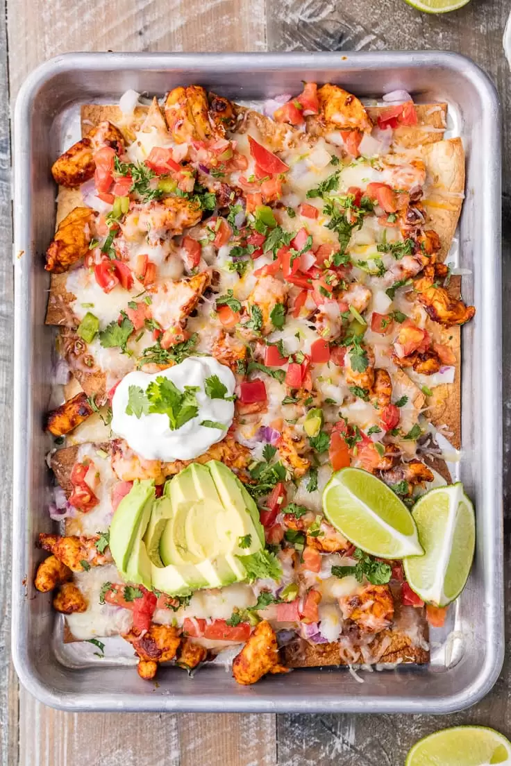Chicken Nachos are great for feeding a crowd! This Tequila Lime Baked Chicken Nachos recipe is just AMAZING! These easy sheet pan nachos are so delicious, and perfect for any occasion. sheet pan nachos made with chicken, pico de gallo, onions, sour cream, avocado, lime, and more