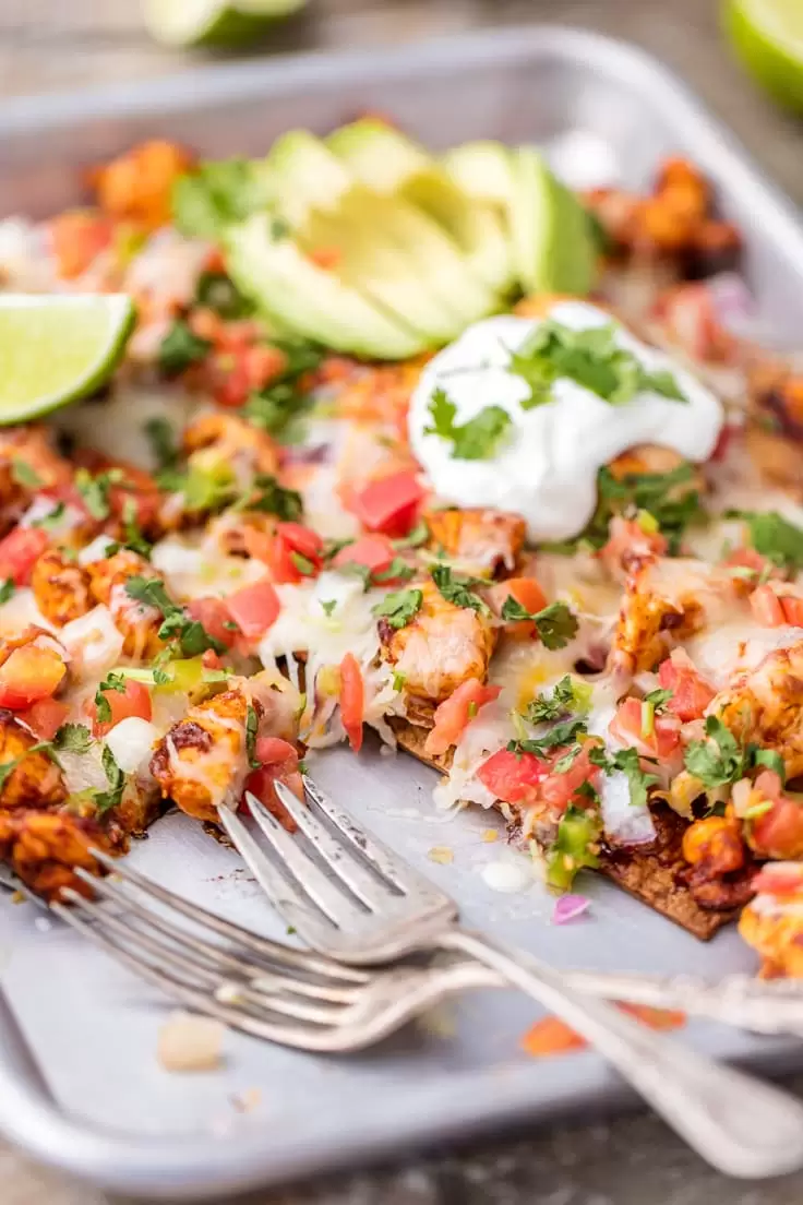 Chicken Nachos are great for feeding a crowd! This Tequila Lime Baked Chicken Nachos recipe is just AMAZING! These easy sheet pan nachos are so delicious, and perfect for any occasion. sheet pan nachos with two forks