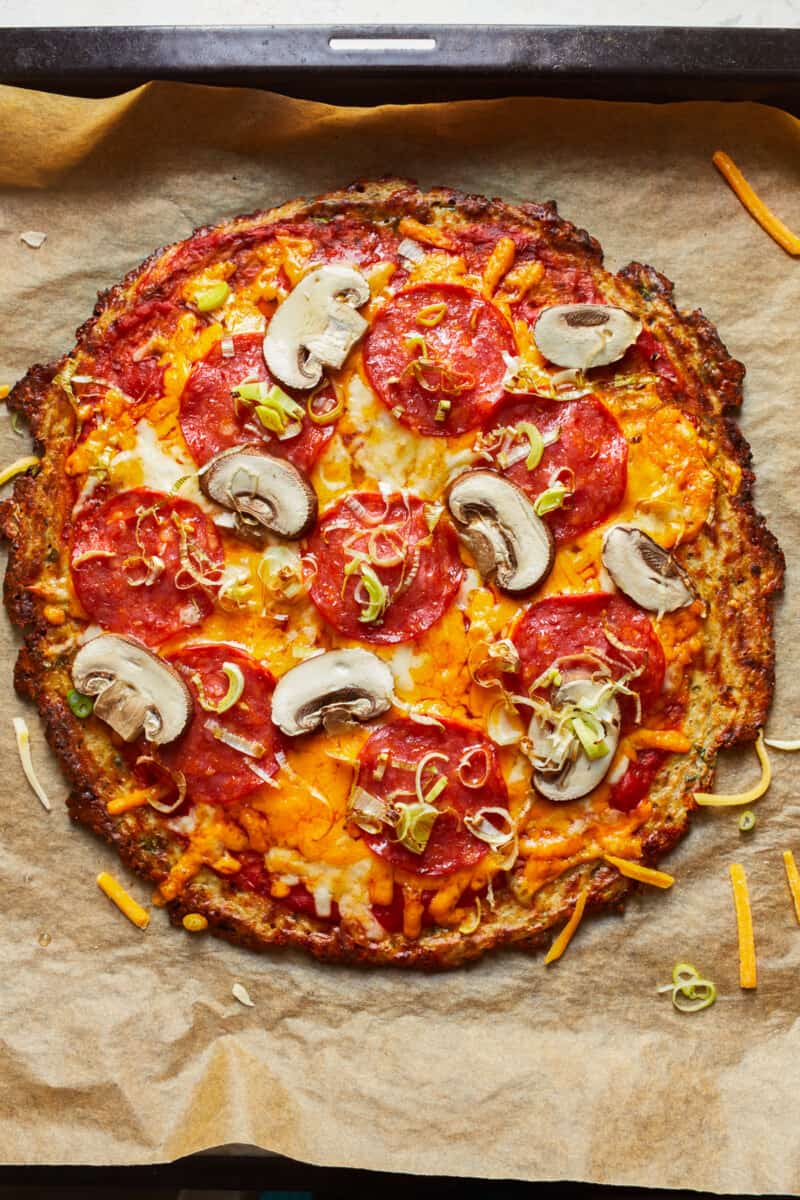 cauliflower pizza crust with pepperoni and mushrooms on parchment