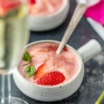 a bowl of strawberry ice cream with a glass of champagne next to it.