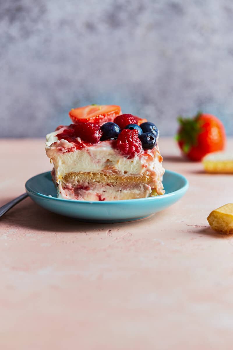 Strawberry Tiramisu with Blueberries and Raspberries is a delicious triple berry dessert! This fruity tiramisu recipe is sweet, beautiful, easy, and SO delicious. It's the perfect easy dessert recipe for Valentine's Day, 4th of July, or any other day of the year! plate with slice of berry tiramisu