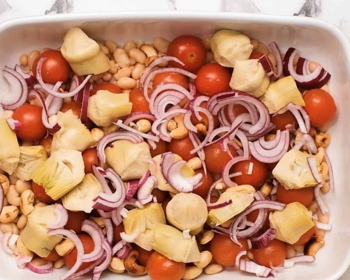 Casserole dish with tomatoes, artichokes, red onion, and cashews.