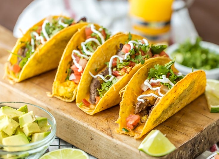 four tacos lined up on a serving board