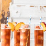 four glasses of iced tea with peach slices and straws.